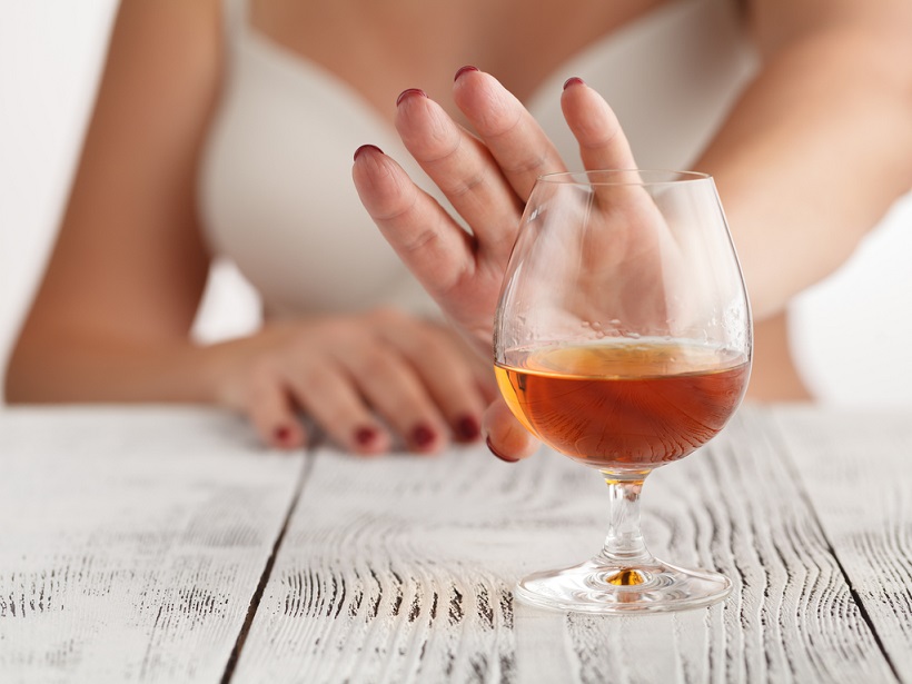 Женщина рукой показывает знак стоп, бокалу с алкоголем